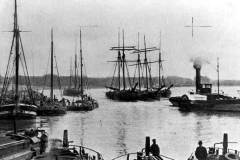 A steam tug towing three sea-going sailing vessels.