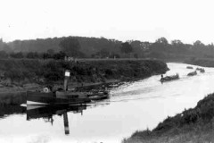 A steam tug towing four fully-laden narrow barges.