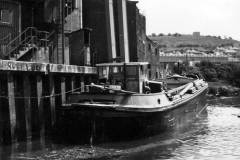 A motor barge berthed on a river.