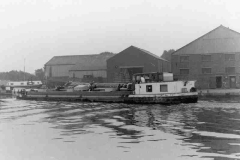A barge passing a warehouse and boatyard.